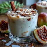 Homemade Guava Coquito served chilled in a small glass with a cinnamon stick stirrer.
