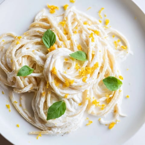 Gelbe Spaghetti in cremiger Ricotta-Soße, verfeinert mit frischer Zitronenschale und Parmesanspänen, liegt appetitlich angerichtet im Teller.  