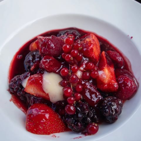 Freshly made Rote Grütze with its juicy berries is presented beautifully, topped with vanilla sauce.