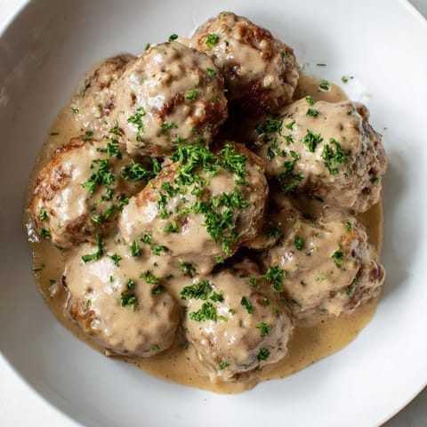 A close-up of delicious Swedish Meatballs with mashed potatoes and bright red lingonberry jam.
