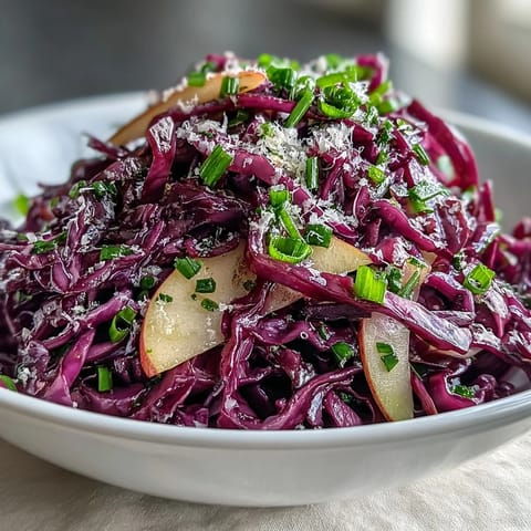 Red Cabbage Coleslaw With Apple and Parmesan tossed in tangy vinaigrette with crisp apple slices visible.